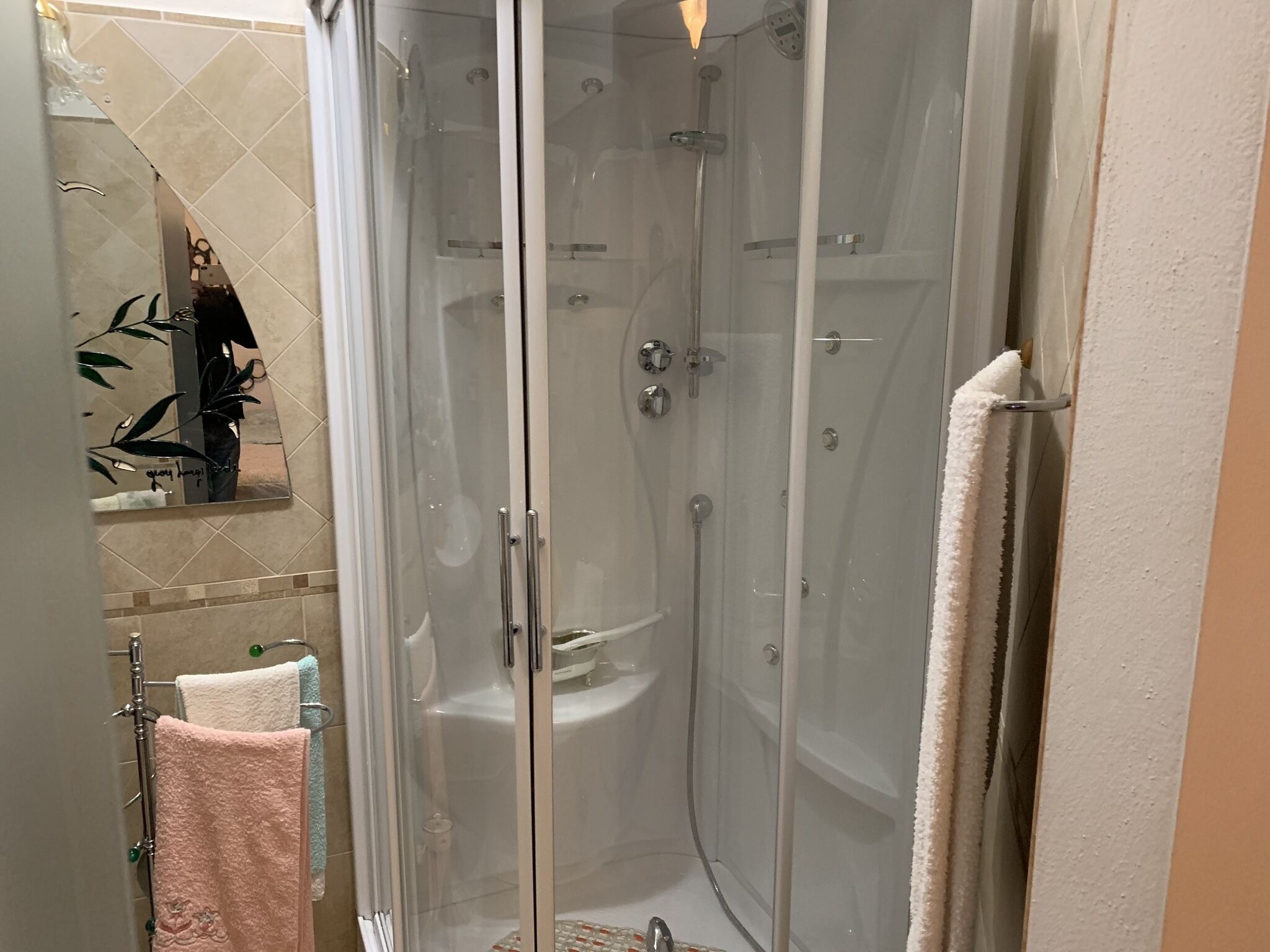 Une cabine de douche fermée par des parois en verre, une baignoire blanche, un porte-serviettes avec plusieurs serviettes et un miroir qui reflète une partie de la salle de bain.