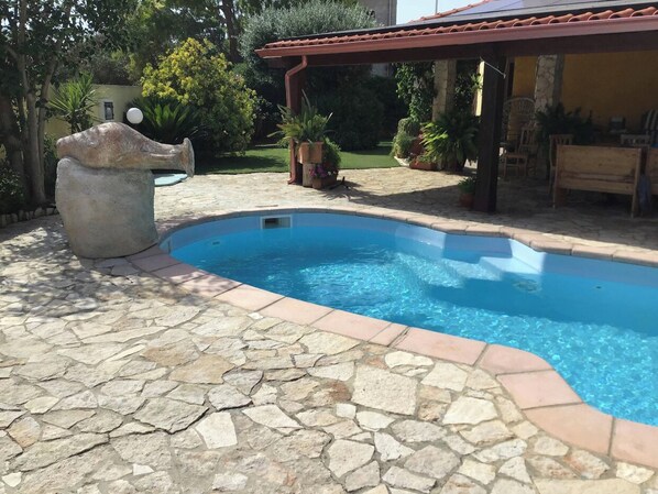 A swimming pool with stone tiles and a pergola in a garden setting.
