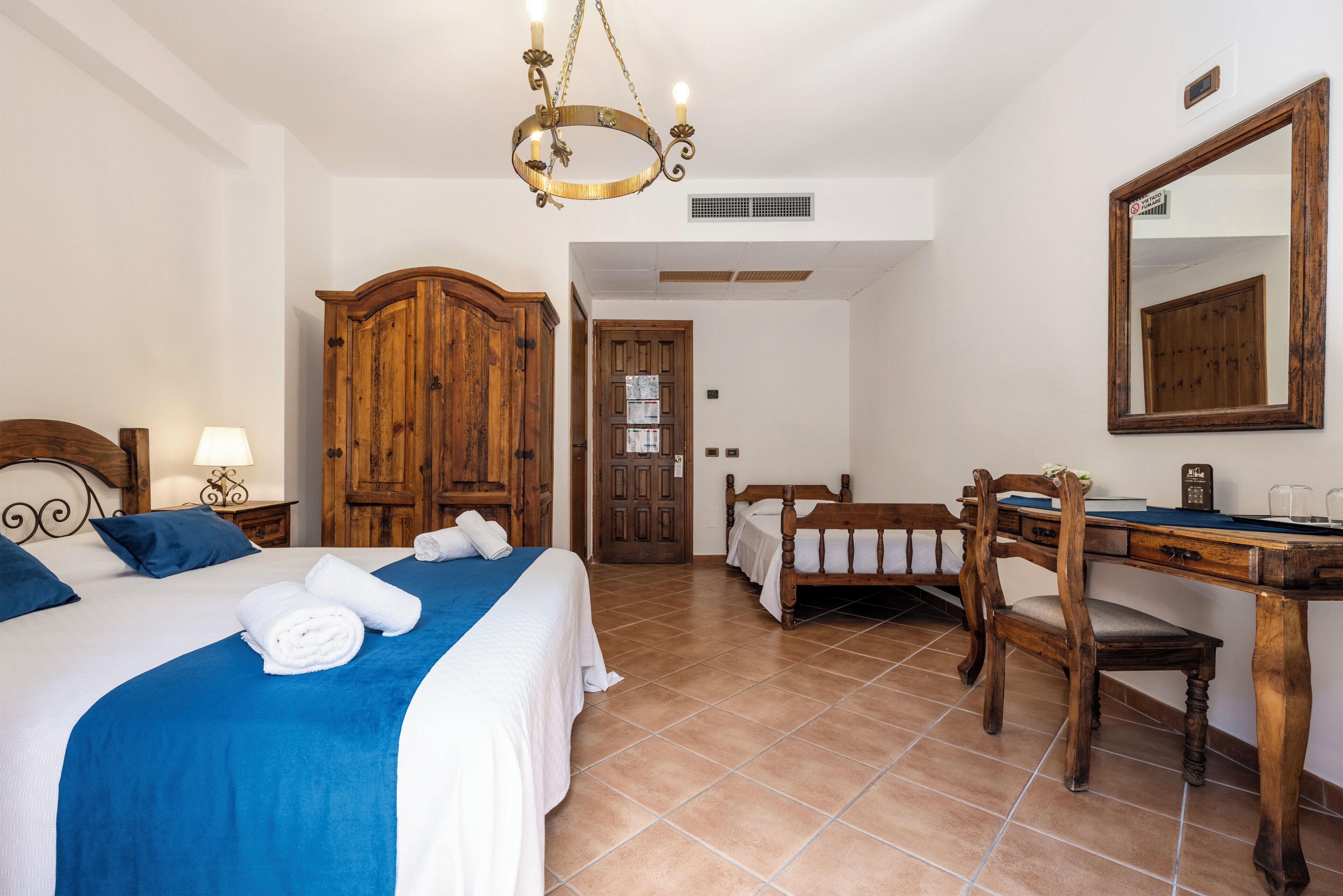 Une chambre d’hôtel avec un grand lit, une armoire en bois, un bureau avec une chaise et un miroir au mur.