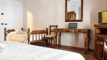 Une chambre à coucher avec un lit, un bureau en bois sur lequel se trouve un ordinateur portable, une télévision et un miroir au mur.