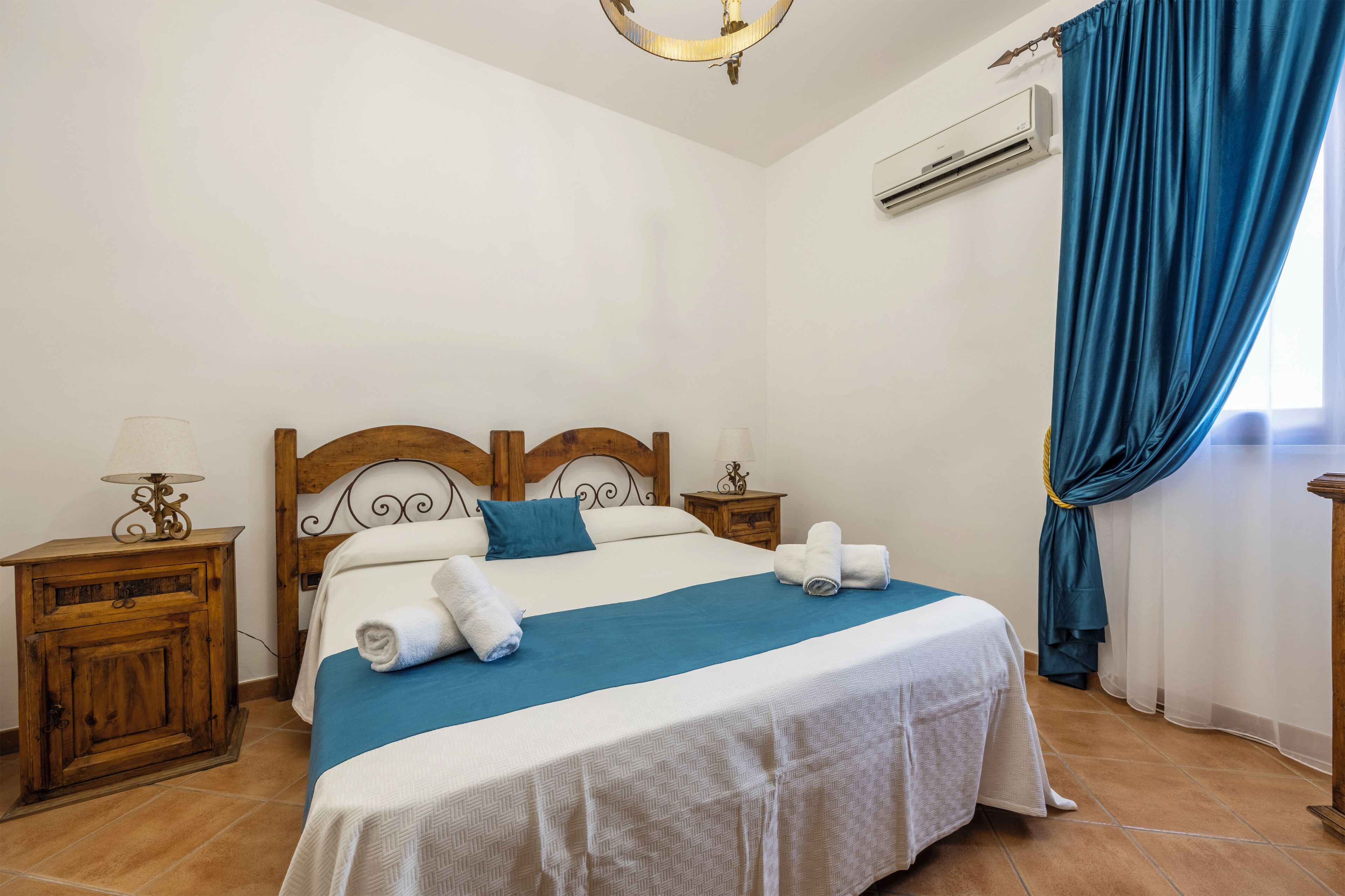 A neatly made bed with a blue and white bedspread, wooden headboard, and two bedside tables with lamps.