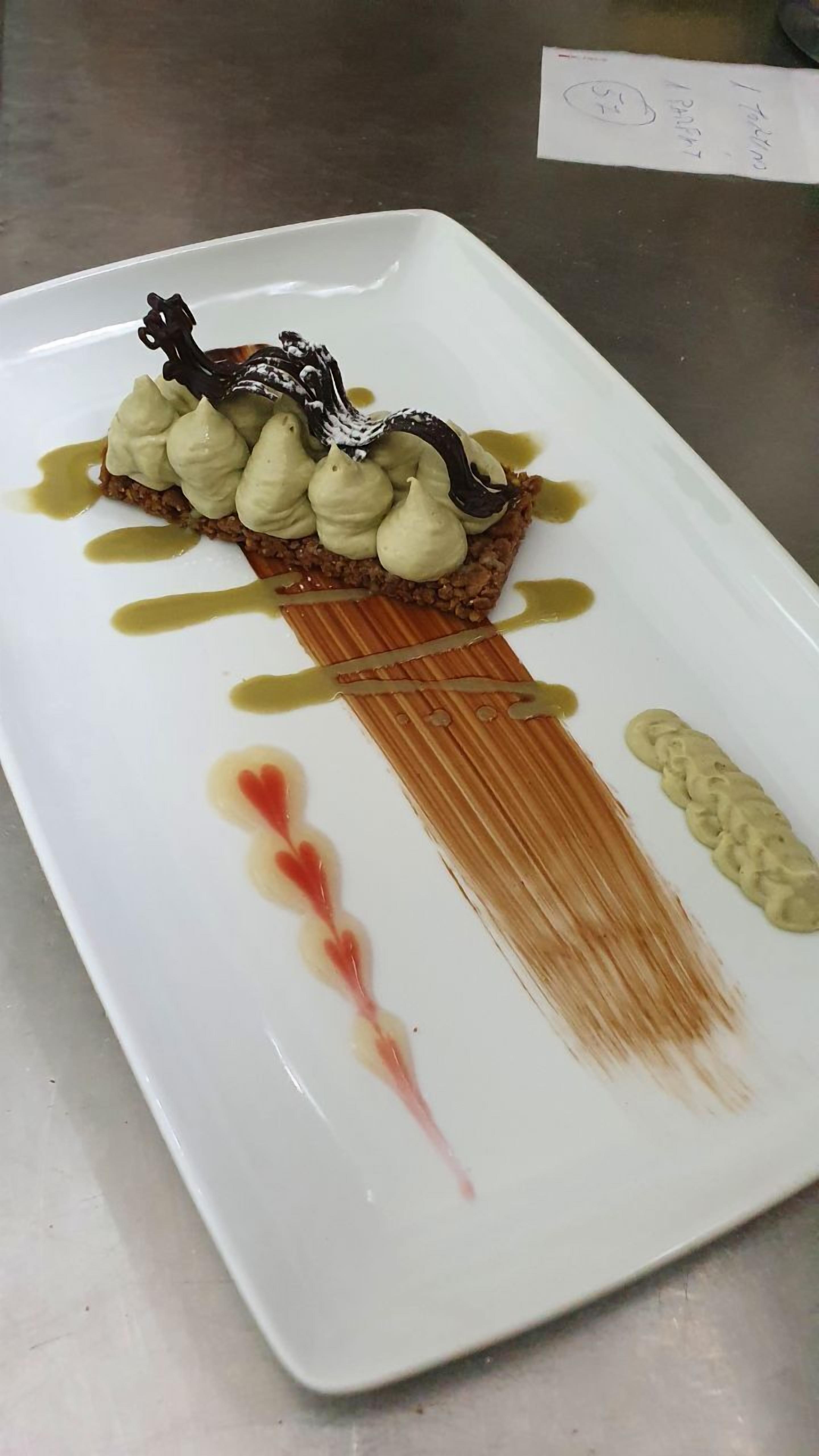 A dessert on a white rectangular plate with a drizzle of sauce and a decorative element.