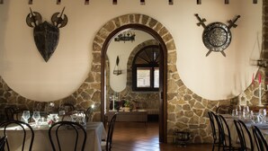 A dining area with stone walls, a shield and ship's wheel decoration, and tables set for dining. - Hotel Castello di Giuliano (Montelepre)