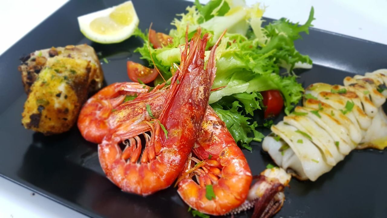 A seafood platter with shrimp, grilled fish, and a side salad on a black plate.