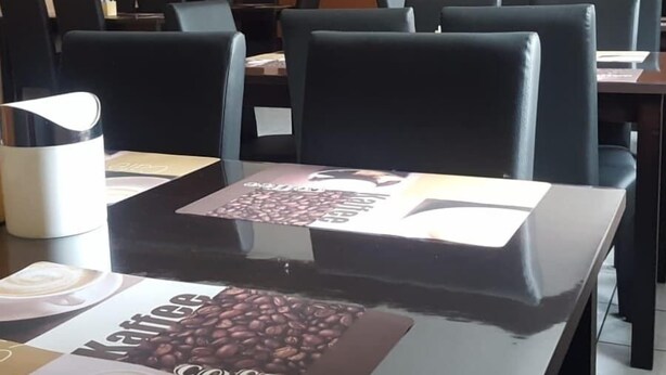 A conference room with tables and chairs, a coffee table with a coffee advertisement, and a painting on the wall. - Euro-Hotel (Saarbrücken)