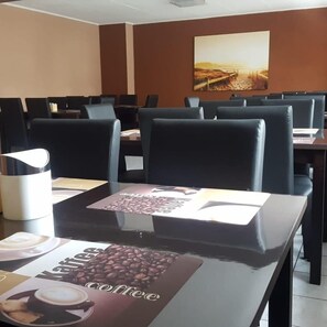 A conference room with tables and chairs, a coffee table with a coffee advertisement, and a painting on the wall. - Euro-Hotel (Saarbrücken)