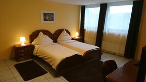 A hotel room with two beds, a desk, a chair, a nightstand with a lamp, a picture on the wall, and a window with curtains. - Euro-Hotel (Saarbrücken)