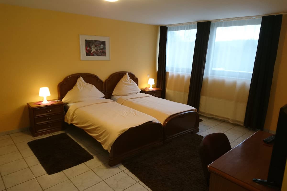 A hotel room with two beds, a desk, a chair, a nightstand with a lamp, a picture on the wall, and a window with curtains.