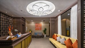 A reception area with a reception desk, a sofa, a coffee table, and a wall with a decorative painting. - Sens House Nha Trang - The Skyline (Nha Trang)