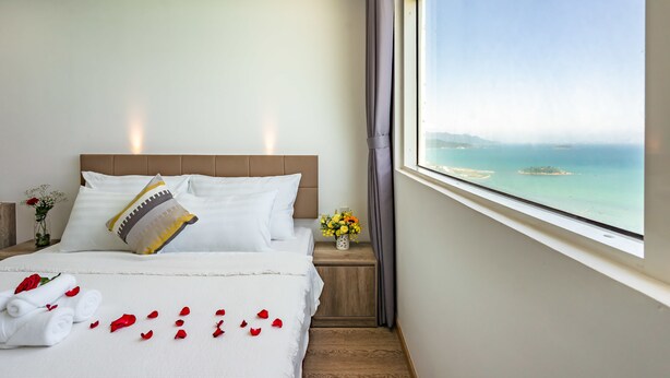 A hotel room with a large bed, a view of the sea, and a window with curtains. - Sens House Nha Trang - The Skyline (Nha Trang)