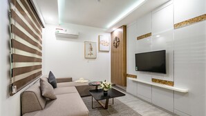 A modern living room with a sectional sofa, a flat-screen TV, a small coffee table with a vase, and a patterned rug. - Sens House Nha Trang - The Skyline (Nha Trang)