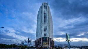 A tall, modern skyscraper with a unique curved design, featuring multiple balconies and a prominent entrance at the base. - Sens House Nha Trang - The Skyline (Nha Trang)