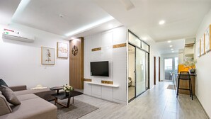 A modern living room with a sofa, coffee table, and TV. There is a hallway leading to a dining area with a chair and table. - Sens House Nha Trang - The Skyline (Nha Trang)