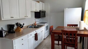 Une cuisine avec des meubles blancs, un four à micro-ondes, une cuisinière, un évier et une table à manger avec des chaises.