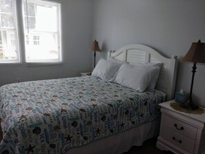 A bedroom with a bed, two bedside tables, a window with blinds, and a patterned bedspread. - Unit C - Pet Friendly! (Orange Beach)