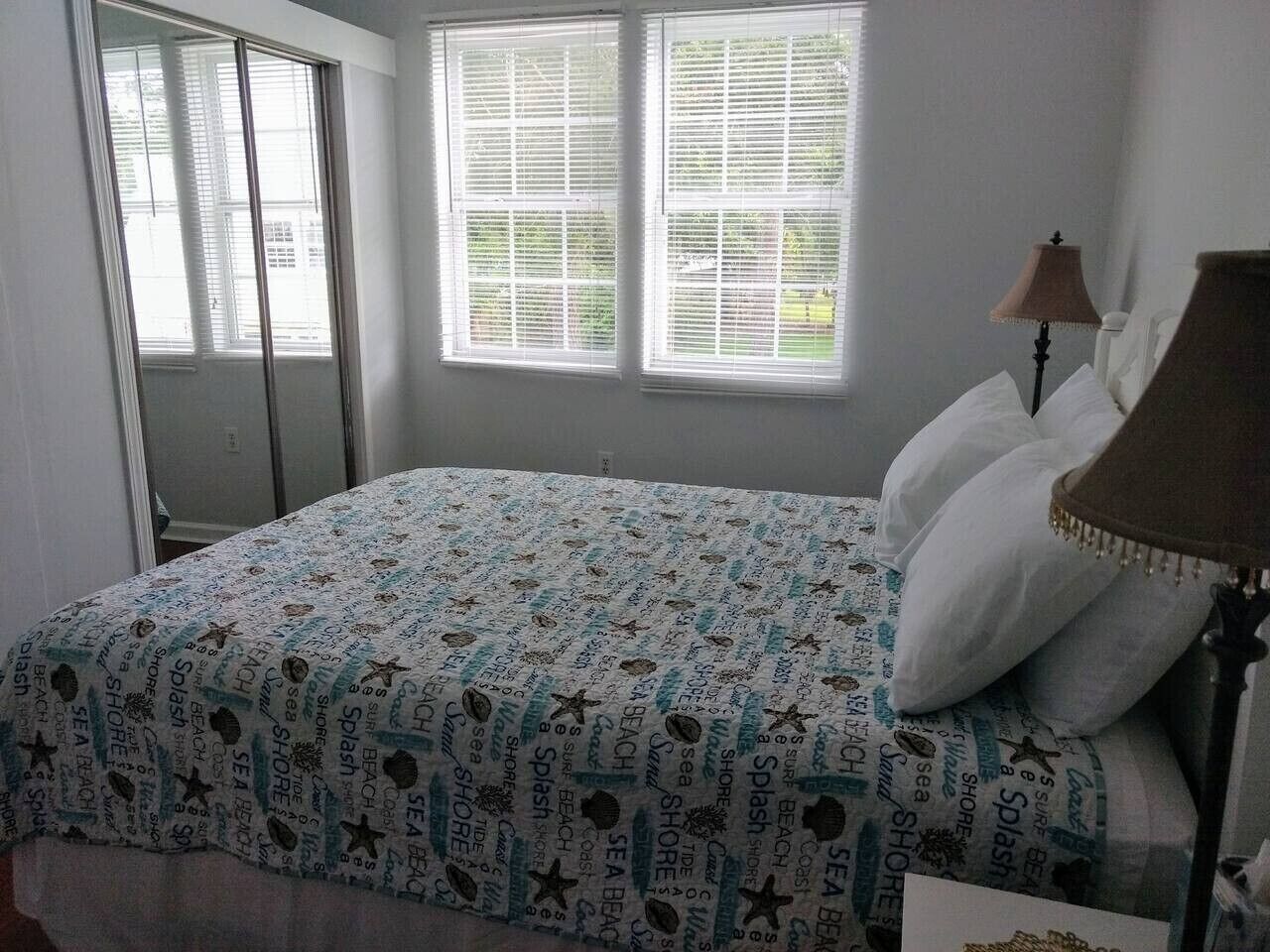 Un dormitorio con cama, una lámpara y dos ventanas con persianas.