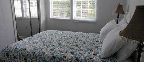 Un dormitorio con cama, una lámpara y dos ventanas con persianas.