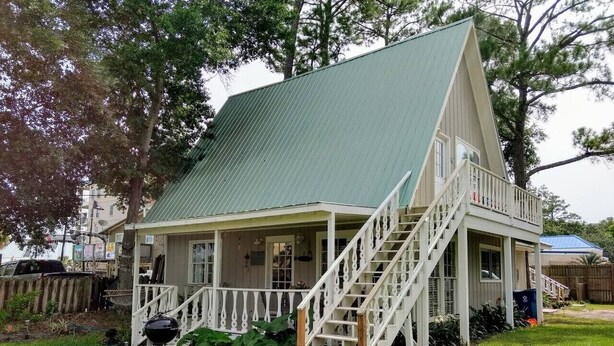 Une maison de plain-pied avec un toit végétalisé, un porche à l’avant doté d’un escalier et un barbecue dans le jardin.