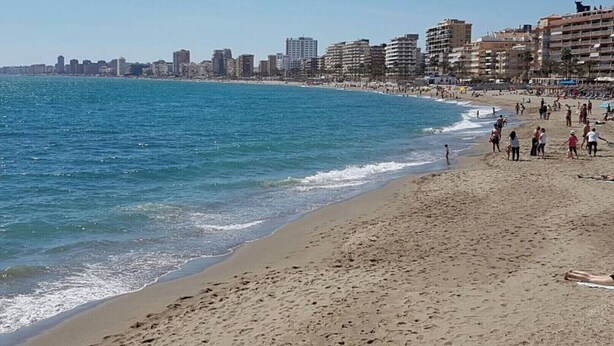 Una playa con el perfil urbano del horizonte, arena y gente disfrutando.