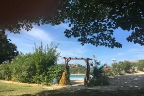 Un jardín con una pérgola, una piscina y cielo despejado.