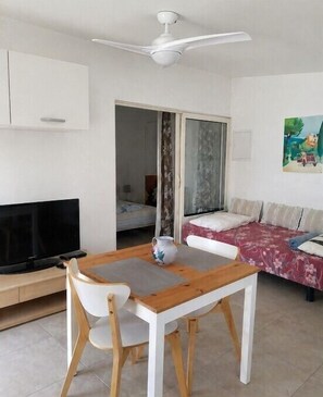 A room with a TV, a table with chairs, a ceiling fan, a sofa, and a painting on the wall.
