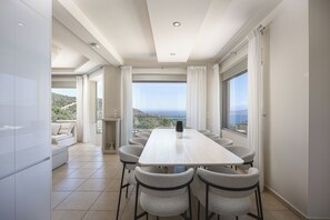 Zona pranzo moderna con un tavolo grande e sedie, ampie finestre con tende e vista sul paesaggio.