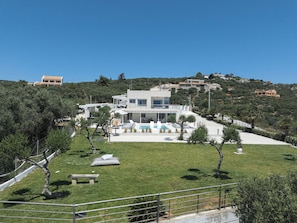 Una casa moderna de dos pisos con piscina, rodeada por un césped cuidado y árboles.