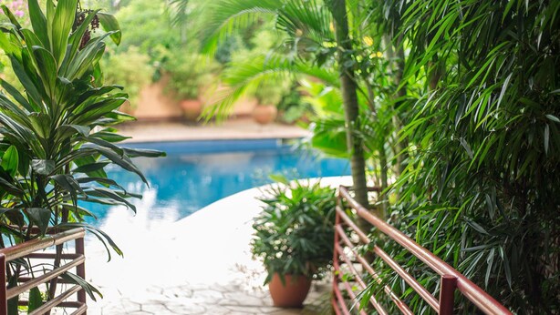 A pool area with a tiled walkway, surrounded by lush greenery and a metal railing. - La Cour Hotel Apartments (Lagos)