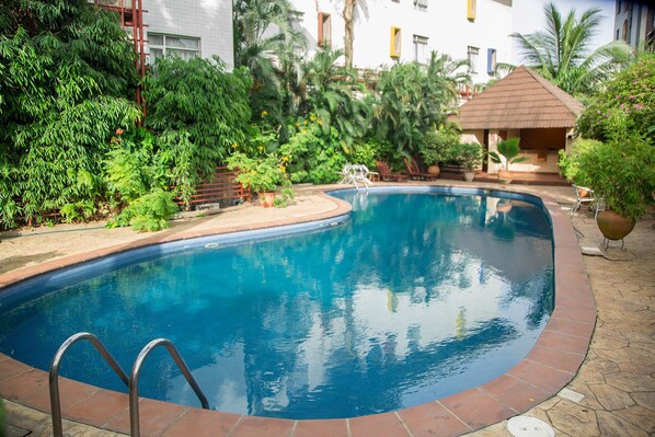 A swimming pool with a metal ladder, surrounded by lush greenery and a small pavilion. - La Cour Hotel Apartments (Lagos)