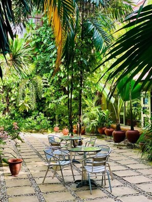 An outdoor patio area with a table and chairs, surrounded by lush greenery and potted plants. - La Cour Hotel Apartments (Lagos)