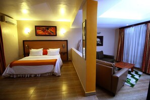 A hotel room with a large bed, a sofa, a small table, and a painting on the wall. - La Cour Hotel Apartments (Lagos)