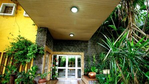 A tropical-style entrance with a stone wall, potted plants, and a wooden ceiling. - La Cour Hotel Apartments (Lagos)