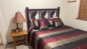 Ein Schlafzimmer mit einem Bett, einem Nachttisch, einer Lampe und einem Fenster mit Jalousien.