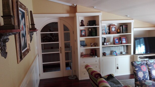 Un soggiorno con un'ampia porta ad arco, una libreria piena di libri e oggetti decorativi, un televisore e un divano con motivo decorativo.