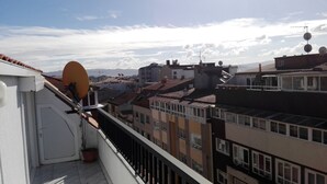 Un balcone con un'antenna parabolica, una pianta in vaso e vista su edifici vicini e montagne.