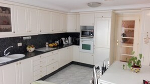 Una cucina compatta con mobili bianchi, un piano di lavoro nero, un lavello, un forno a microonde e un fornello. È presente un piccolo angolo ristoro con un tavolo e sedie.
