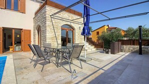 An outdoor patio with a stone table and chairs, a pool, and a stone building with wooden shutters. - Charming 3-BR villa with private pool close to beaches (Novigrad)