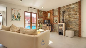 A living room with a beige sofa, a TV, a fireplace, and a stone wall. - Charming 3-BR villa with private pool close to beaches (Novigrad)