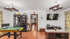 Een woonkamer met een pooltafel, een bank, een kast met decoratieve objecten en een aan de muur bevestigde televisie.