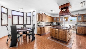 Een keuken met houten kastjes, een centraal eiland en een eethoek met stoelen.
