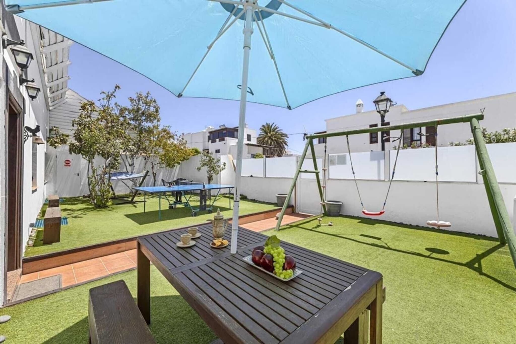 A patio with a wooden table, a swing set, and a large umbrella.