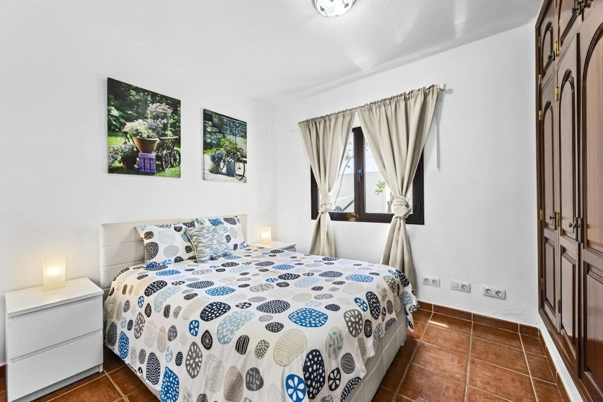 A bedroom with a bed, nightstand, and two wall-mounted pictures.