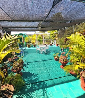 Relax by the pool surrounded by lush greenery and shaded by a large umbrella.