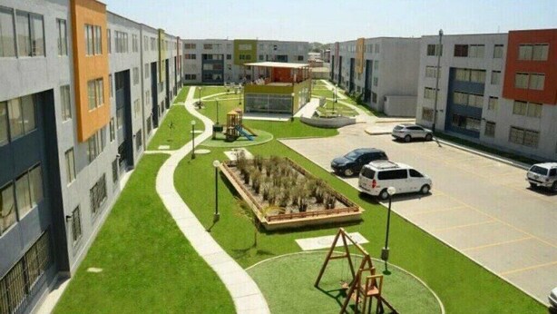 Un edifici residencial modern amb un pati central, gespa verda i una zona d'aparcament.