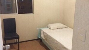 Habitació petita amb un llit individual, una finestra, una cadira i una porta.