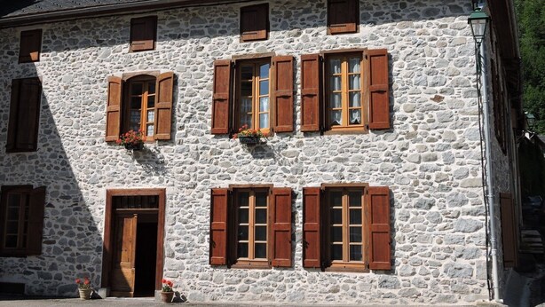 Un edificio in pietra con diverse finestre e persiane di legno.