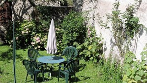 Un giardino con un tavolo rotondo e quattro sedie, immerso nel verde e tra piante fiorite.