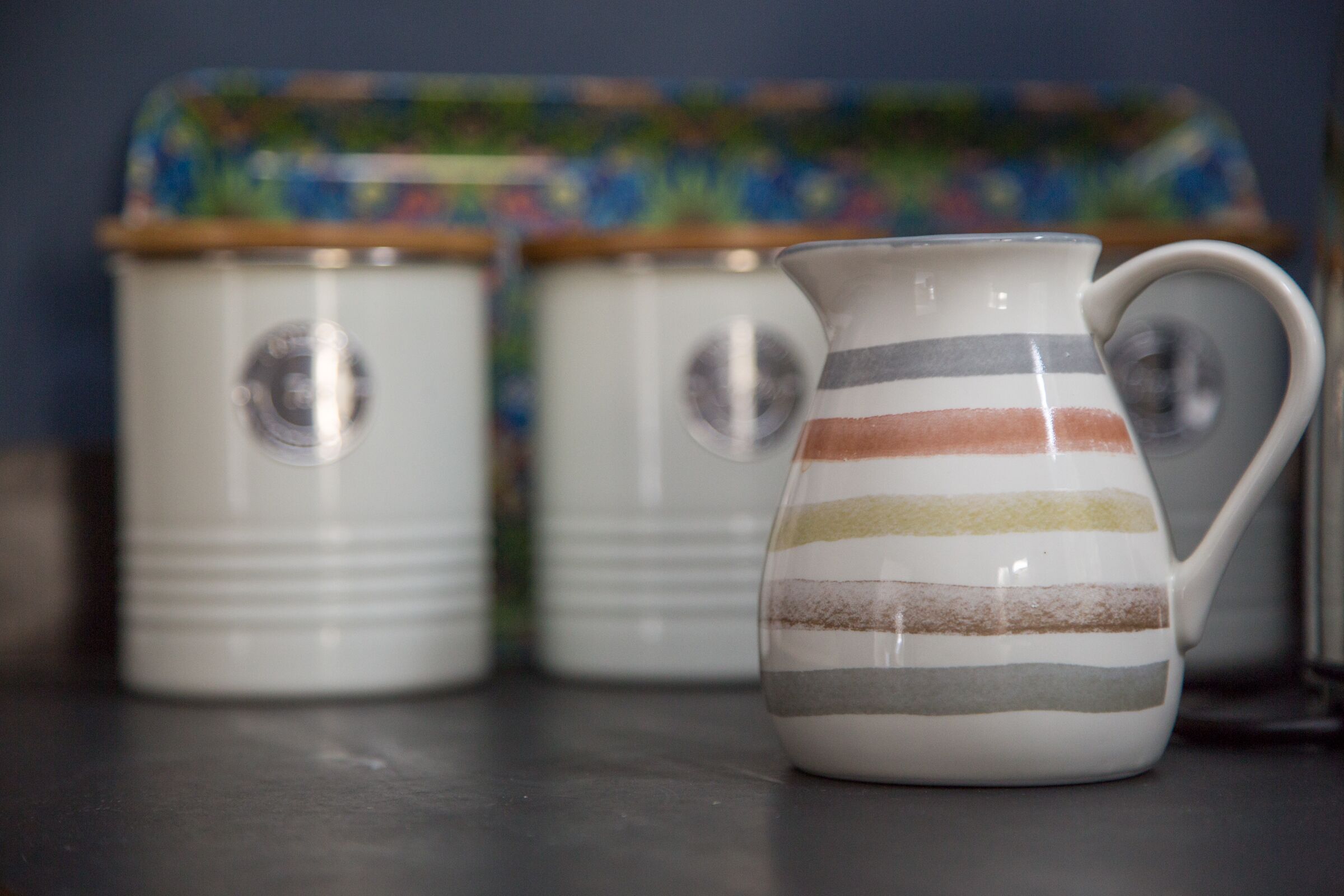 Three white ceramic containers with striped patterns and handles, placed on a dark surface.
