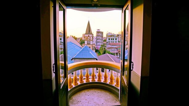 A view from a balcony with a railing, overlooking a cityscape with buildings and a church spire. - Royal Ruby Hotel (Mandalay)