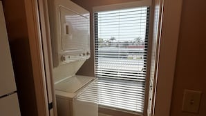 A compact kitchen with a built-in oven, a washing machine, and a window with blinds. - Second Story Garden unit, Sleeps 6! (Sarasota)